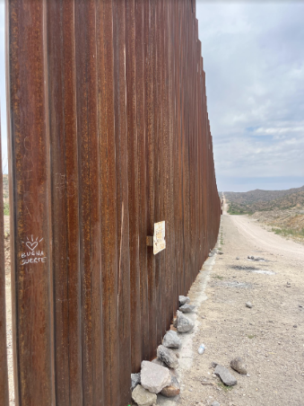 A close-up view of the gated border wall between U.S. and Mexico. One of the gate poles has a small drawing of a heart and the words 